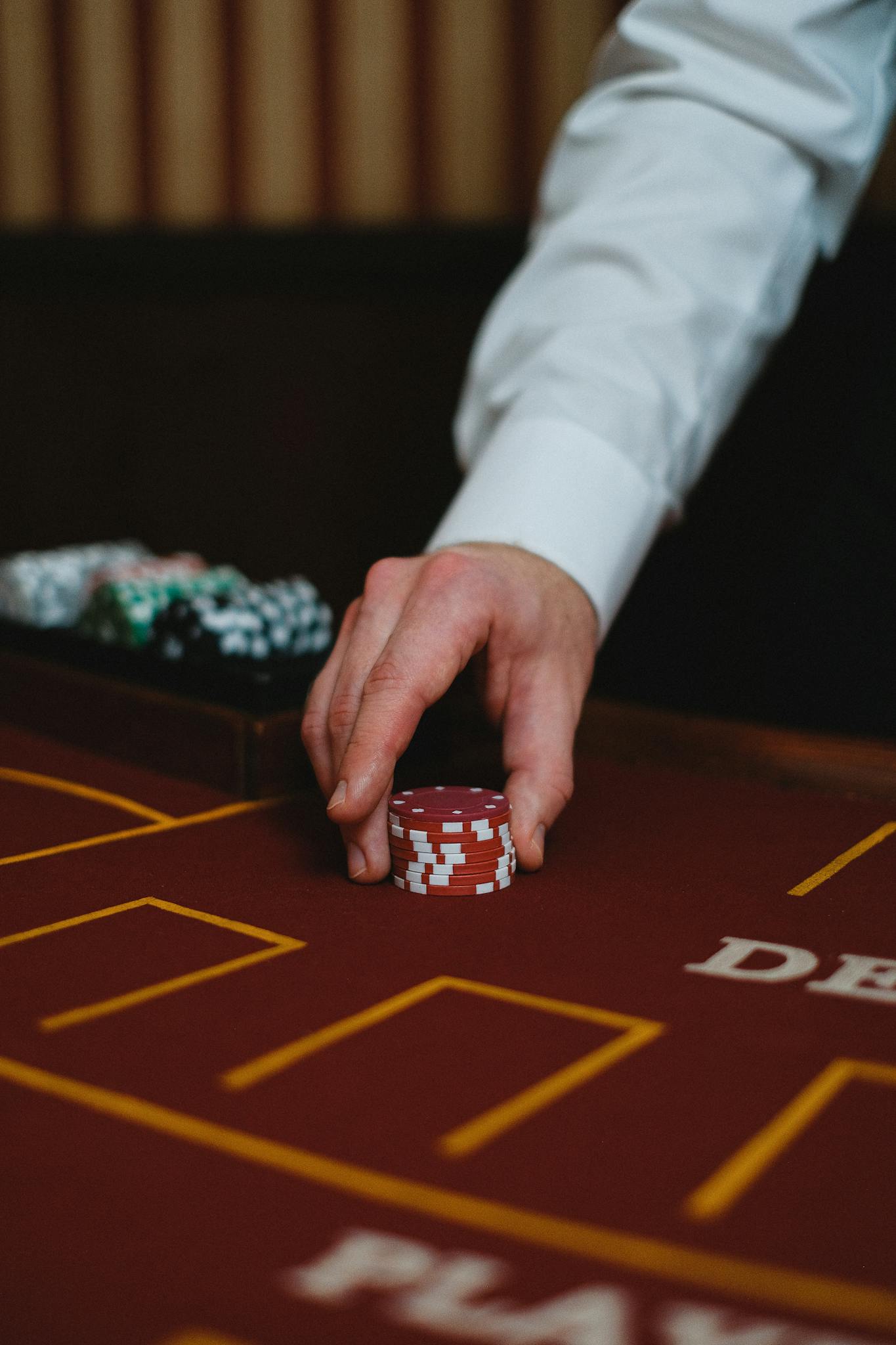 A dealer's hand holding red poker chips on a casino table, ready to play.