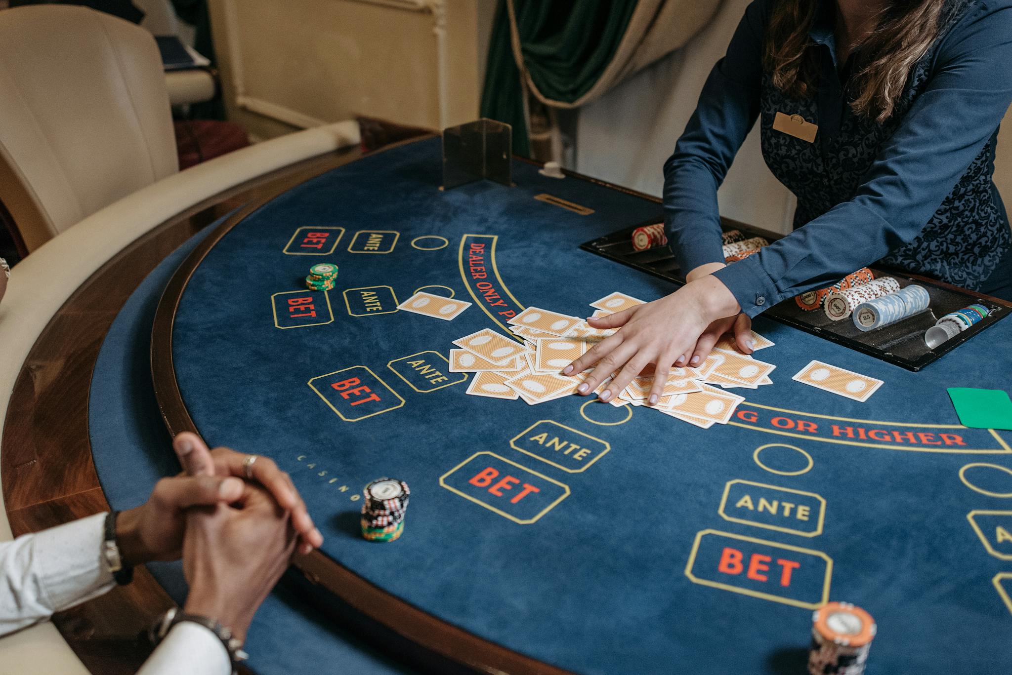 Close-up of a casino dealer shuffling cards on a gambling table with chips and bet labels.